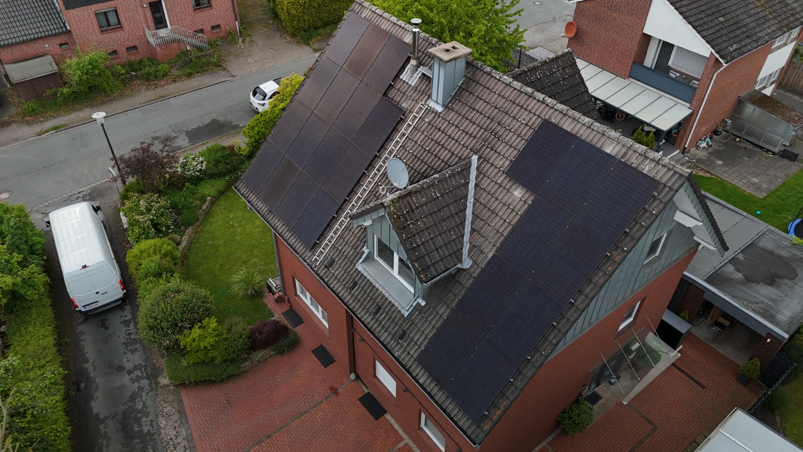 Luftaufnahme der Photovoltaik-Montage auf einem Klinkerhaus mit Dachleiter und Montagefahrzeug
